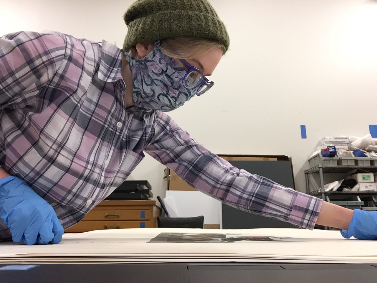 A woman wearing blue nitrile gloves measures an Audubon print of widgeons