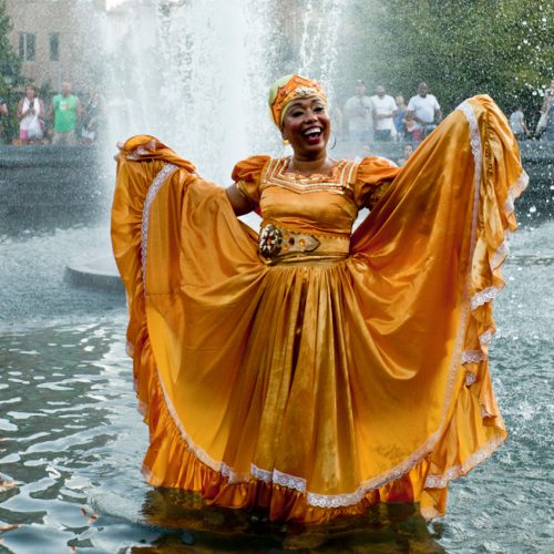 Photo of Yesenia Selier standing in a fountain wearing a yellow dress
