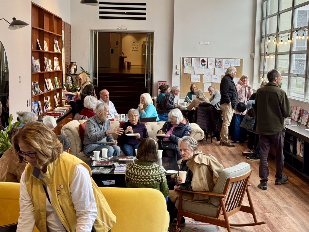 Members gather around tables and on couches chatting and drinking coffee