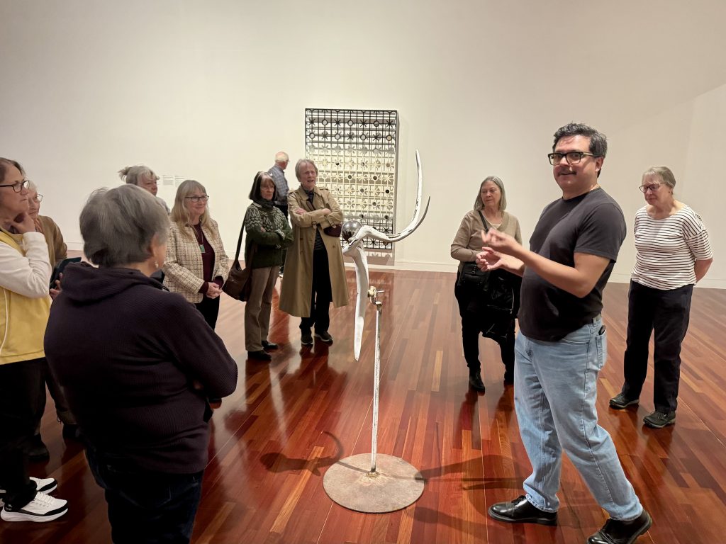Members gather around an art piece formed from an antler on a stand
