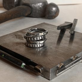 a set of 4 stacked silver rings with metal stamping tools and a hammer sitting nearby