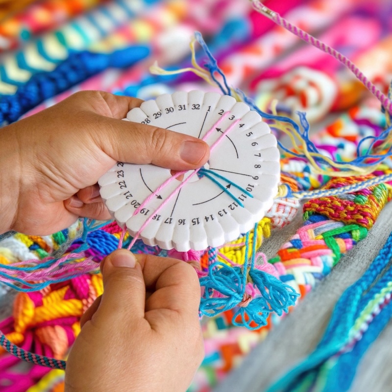 someone creates colorful braided cords with a disk loom