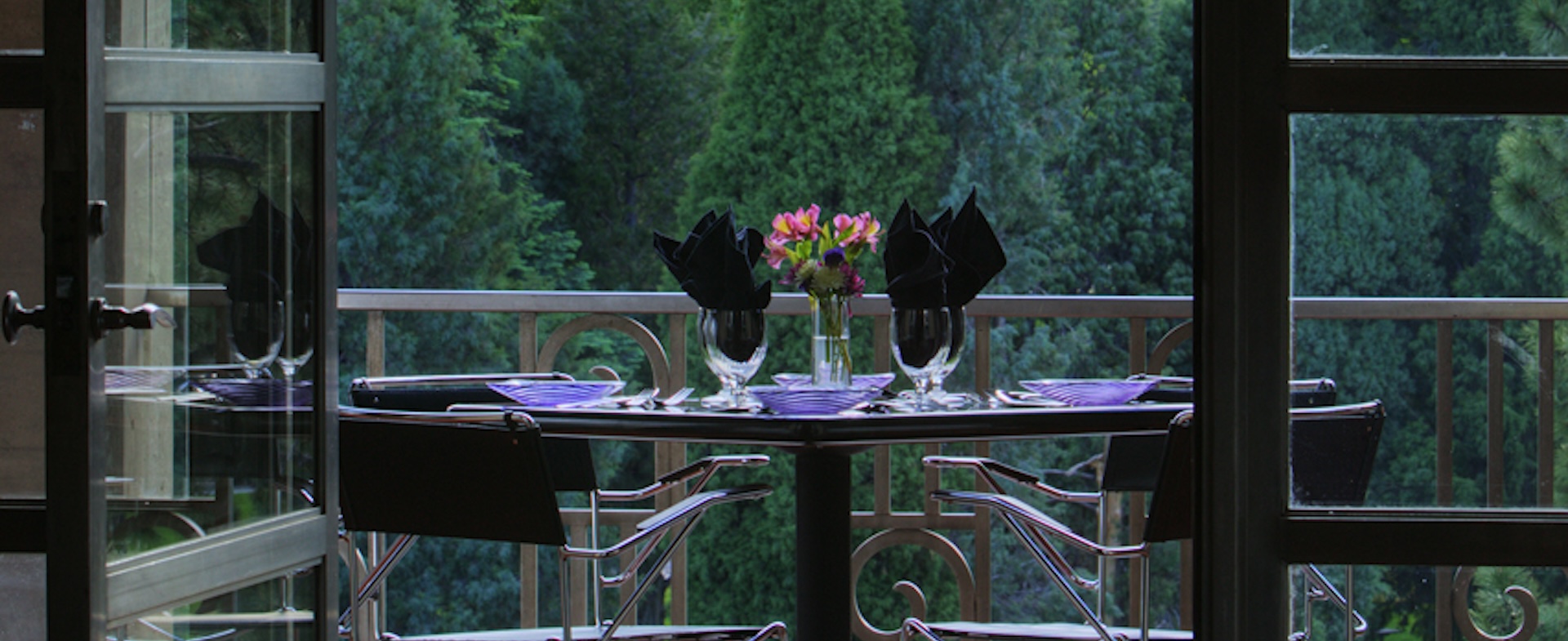A dining table formally set on a balcony overlooking a view of trees