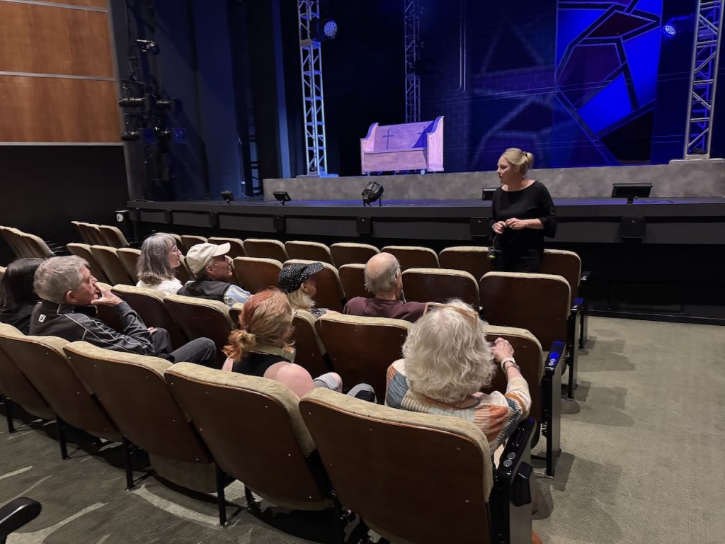 members sit in the theatre seats and listen to a presentation given from in front of the main stage