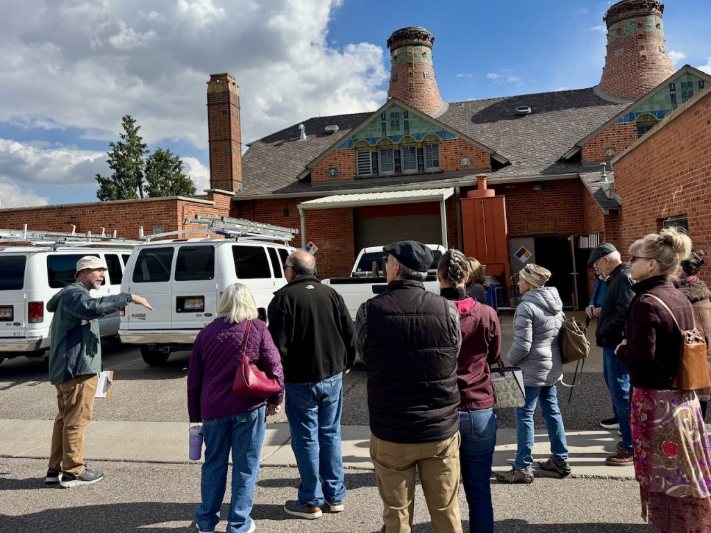 members stand outside and listen to a presentation on the Van Briggle building which is visible in the background