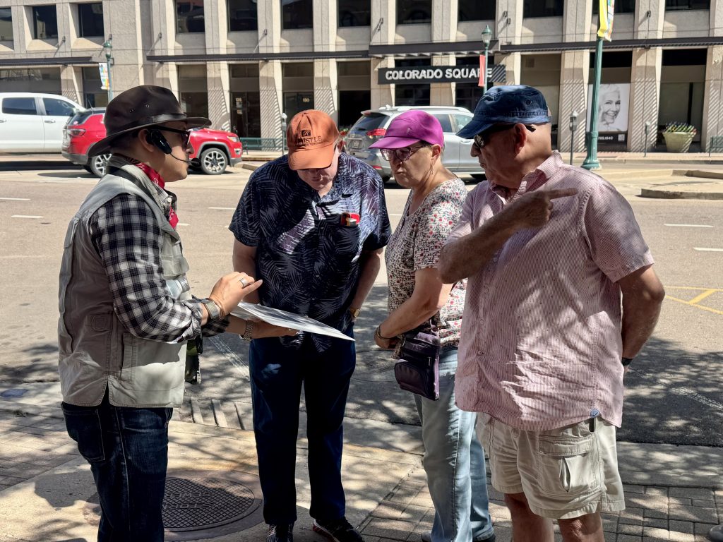 tour guide shows group of members information he is holding on a sidewalk in downtown