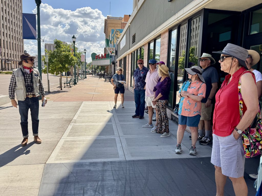 tour guide talks to group of members on a sidewalk downtown