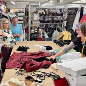 Costume director shows gathered members a costume backstage