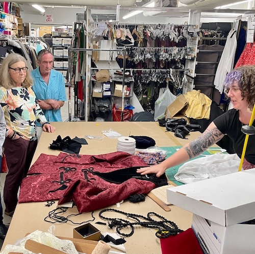 Costume director shows gathered members a costume backstage