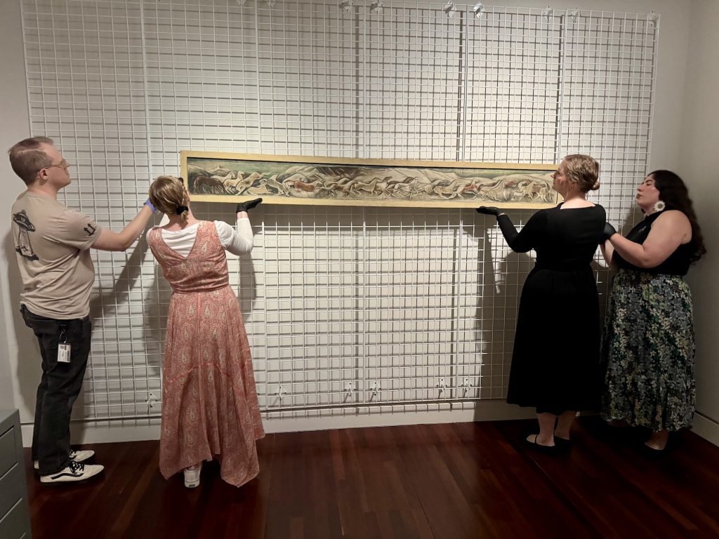 Museum workers wearing gloves mount the Mechau piece to the wall