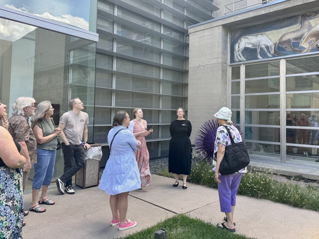 Members stand outside the Fine Arts Center and listen to a presenter