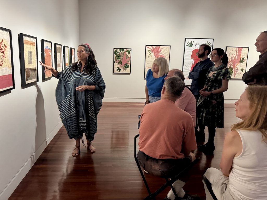 Members look on as a docent points something out in an artwork hanging on the wall