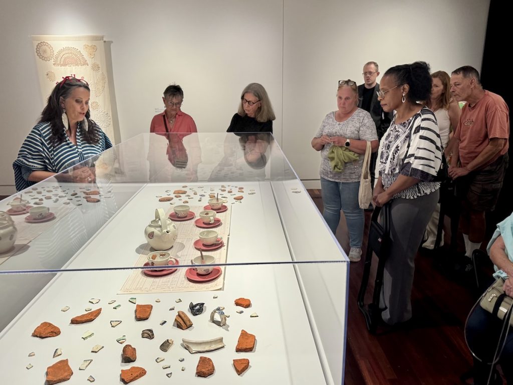 Members gather around several art pieces in a glass case