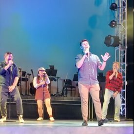 Four people sing karaoke from a stage