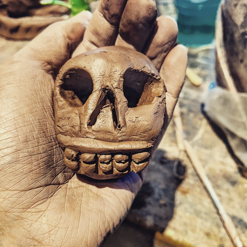 A hand holding a wet clay skull